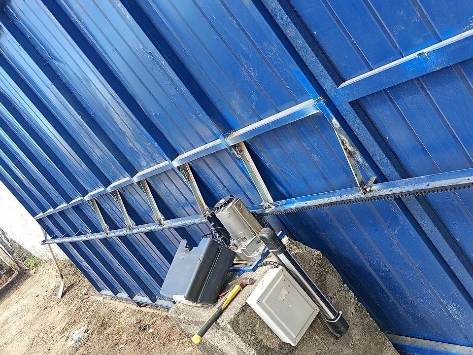 Portão grande de chapa azul com reforços soldados em travessas e diagonais, cremalheira nova e motor sendo instalado